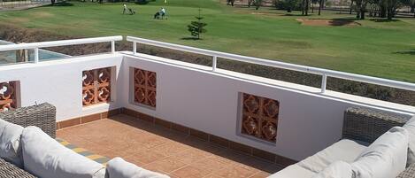 Terraza en la azotea con mobiliario de mimbre y vistas a un campo de golf.