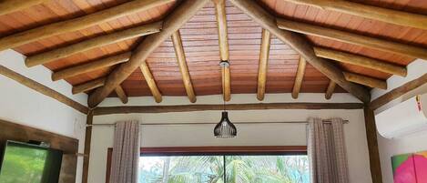 Een kamer met houten plafond, een hanglamp en een raam met gordijnen.