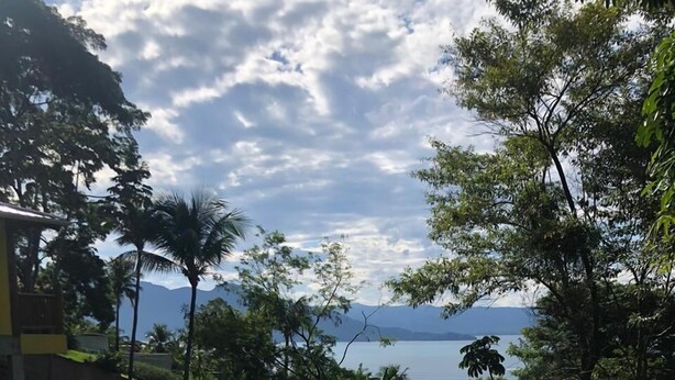 A rectangular swimming pool with clear blue water, surrounded by greenery and a view of a body of water and mountains in the distance. - Siriúba Reserve (Ilhabela)