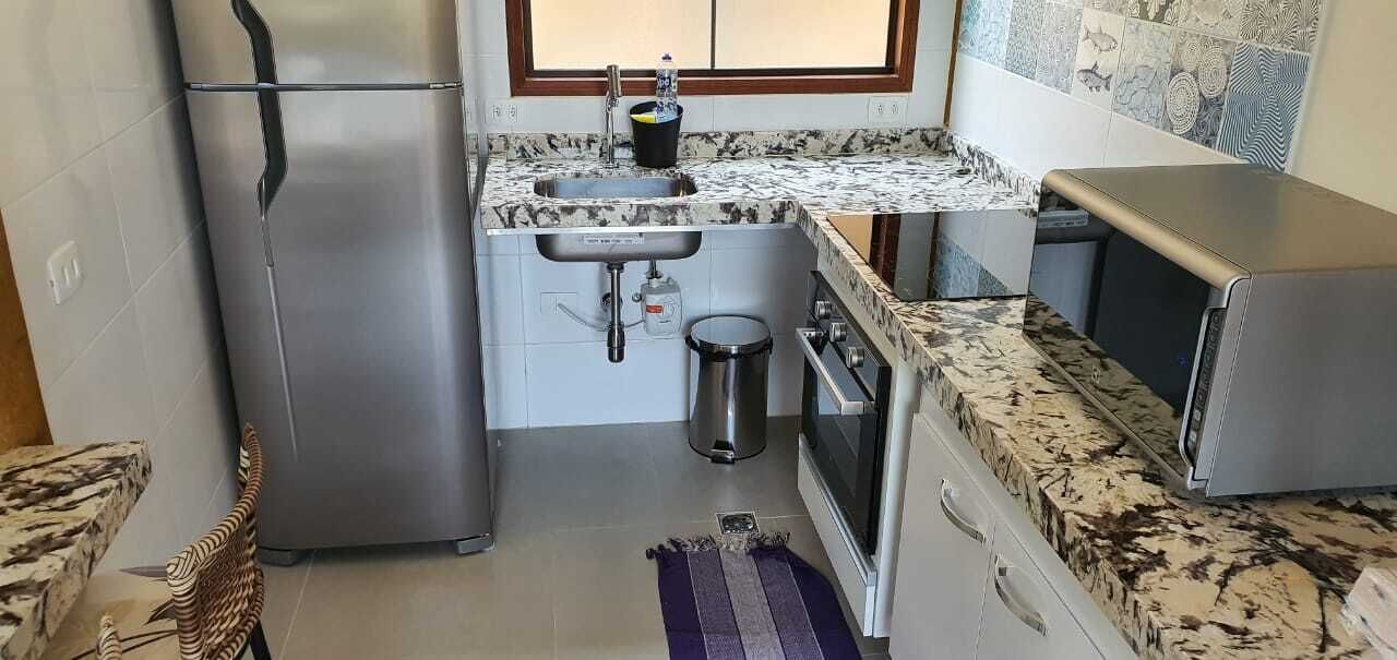A compact kitchen with a stainless steel refrigerator, a sink, a stove, and a microwave.