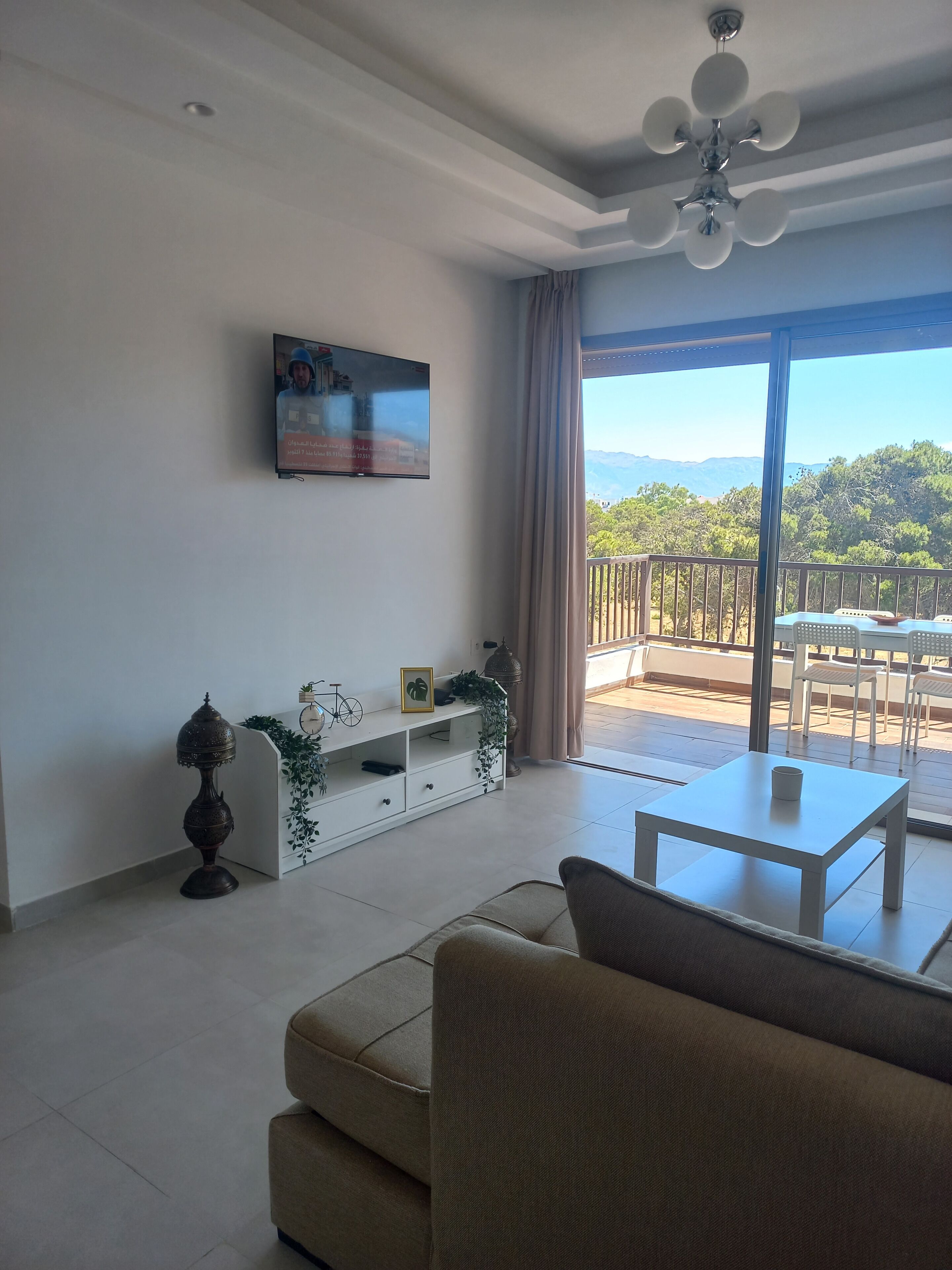 Un salon comprenant un canapé, un téléviseur fixé au mur, un ventilateur de plafond et un balcon aménagé avec du mobilier d’extérieur.