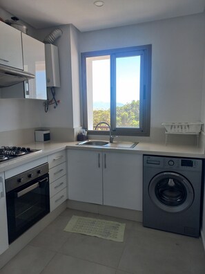A modern kitchen with white cabinets, a gas stove, a built-in oven, a sink, and a front-loading washing machine. - Quiet spot in Cabo negro (Cabo Negro)