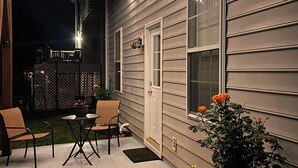 Een terras buiten met een tafel en stoelen, een kleine tuin met planten, en een houten pergola met lichtslingers.