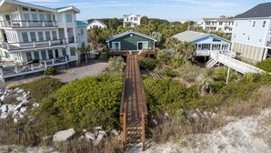 A coastal property with a wooden deck leading to a house, surrounded by lush greenery and other buildings.