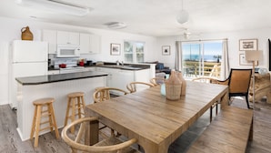 Een moderne keuken met witte kastjes, een houten eettafel en uitzicht op de oceaan.