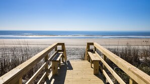 A wooden boardwalk leading to a beach with benches and a clear view of the ocean.
