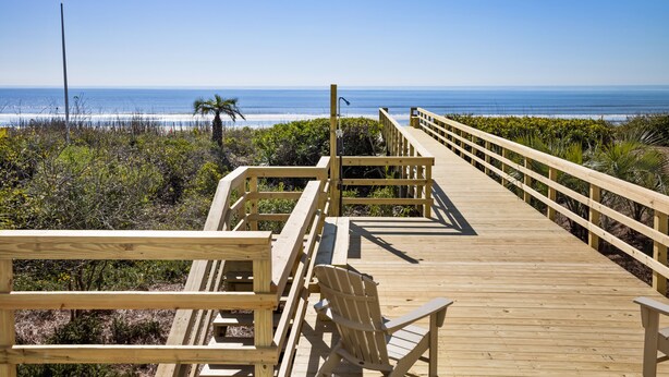 A wooden boardwalk leading to a beach with a chair and a lamp post.