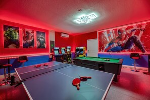 Una habitación con mesa de ping pong, juegos de arcade y mesa de billar.