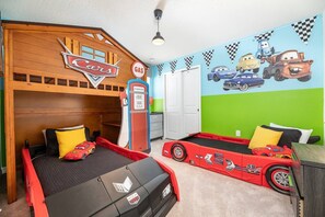 Un dormitorio infantil con una cama litera, un área de juegos con coches de juguete y un mural temático de carreras.