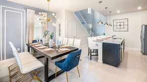 A modern kitchen with a central island, a dining area with a dark wood table, and a staircase leading to an upper level. - Family Fun Oasis|Arcade|Game Room|FREE Pool Heat (Davenport)