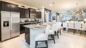 A modern kitchen with dark cabinets, stainless steel appliances, a central island with white bar stools, and pendant lighting. - Family Fun Oasis|Arcade|Game Room|FREE Pool Heat (Davenport)