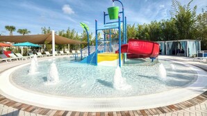 A water play area with slides and fountains, surrounded by lounge chairs and umbrellas. - Family Fun Oasis|Arcade|Game Room|FREE Pool Heat (Davenport)