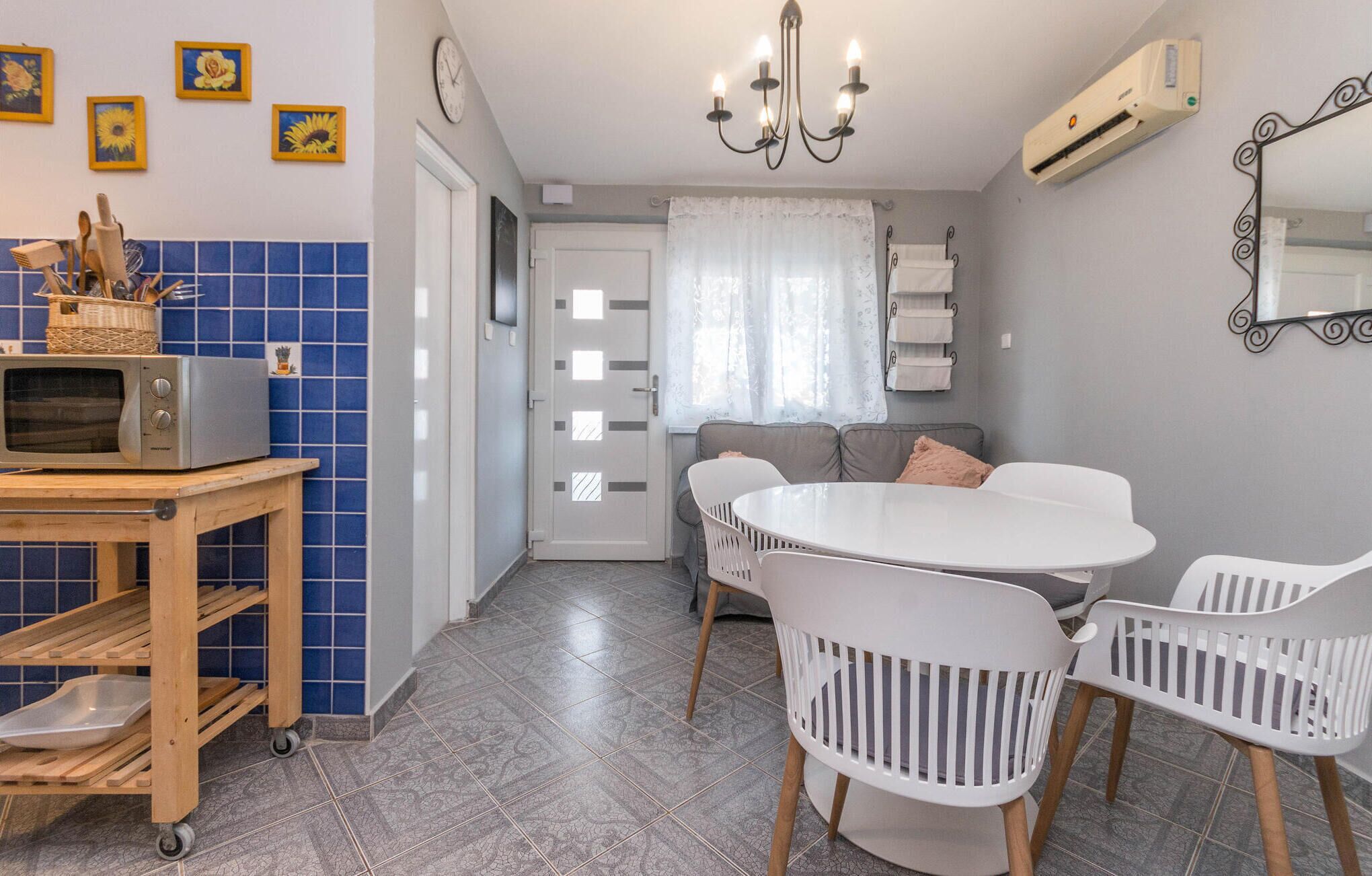 A compact kitchen with a microwave, a wooden cart, and a dining area with white chairs and a round table.