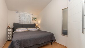 Un dormitorio con cama, mesita de noche, lámpara, espejo y ventana con cortinas.