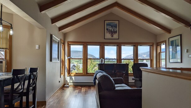 A spacious living area with a high ceiling, wooden beams, a sofa, a dining table with chairs, and large windows offering a view of the mountains. - Spacious In-Town Condo | Pool | Hot Tub (Durango)