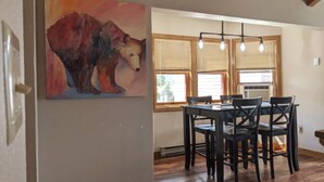 A dining area with a wooden table and chairs, a painting of a bear on the wall, and a window with blinds. - Spacious In-Town Condo | Pool | Hot Tub (Durango)