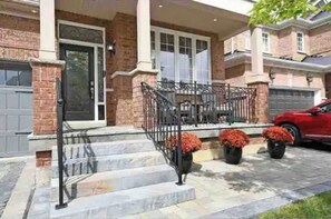A two-story house with a brick facade, a front porch with steps, and a red car parked in the driveway.