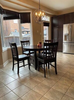 A dining area with a round table and six chairs, a chandelier, and a view of the outside through large windows.