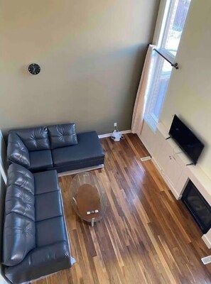 A living room with a sectional sofa, a glass coffee table, a flat-screen TV, and a radiator.