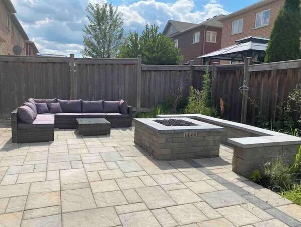 A patio area with a sectional sofa, a fire pit, and a stone planter.