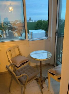A balcony with a glass door, two chairs, a small round table, and a view of a cityscape.