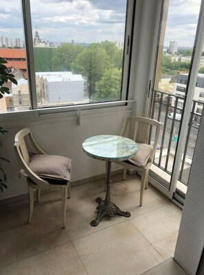 Un balcón con una pequeña mesa, dos sillas, vistas de la ciudad y una planta a la izquierda.