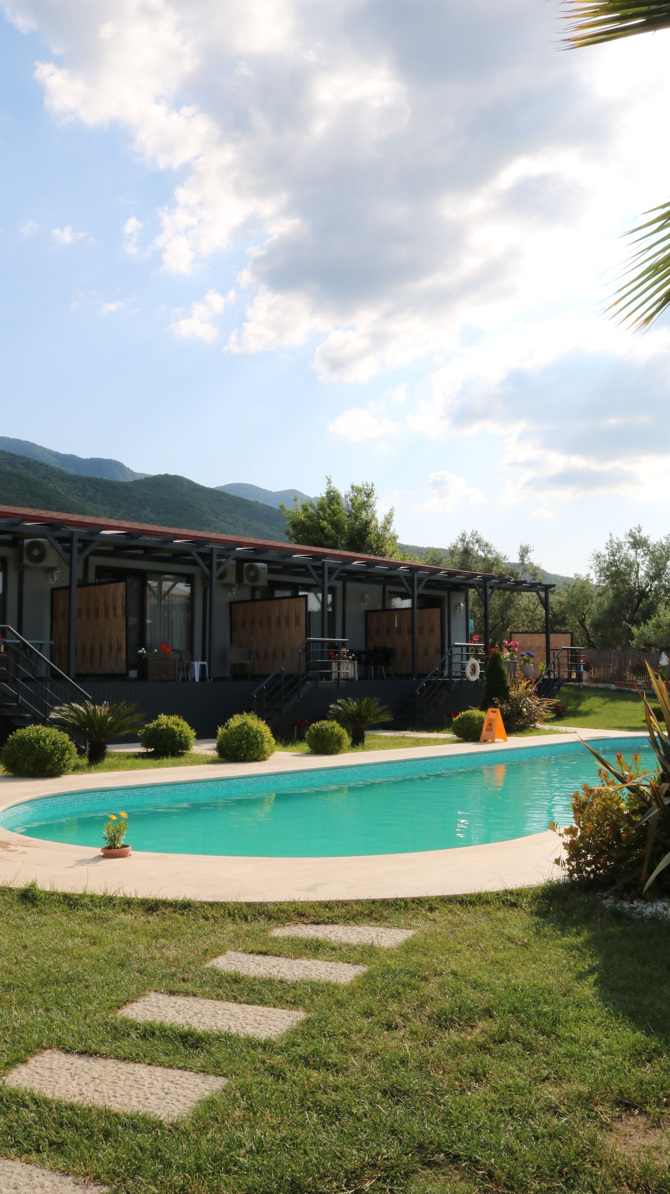 Ein Poolbereich mit überdachter Terrasse, Treppe zum Pool und Blick auf Berge im Hintergrund.