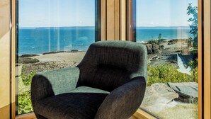 Een moderne kamer met een groot raam dat uitzicht biedt op de oceaan en de rotsachtige kustlijn.