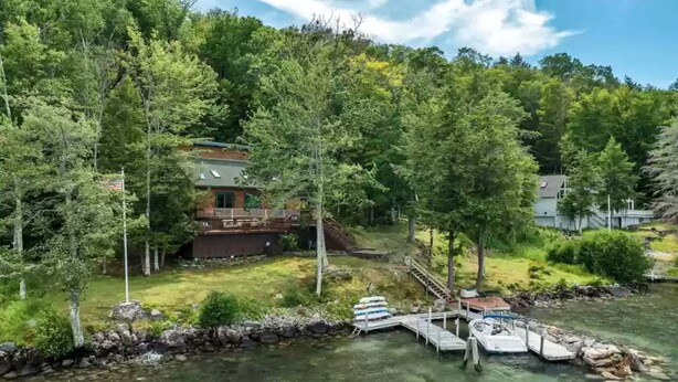 A lakeside cabin with a deck, surrounded by dense forest and a dock extending into the water. - Waterfront at Winnipesaukee with incredible views!! Boat Required (Alton)