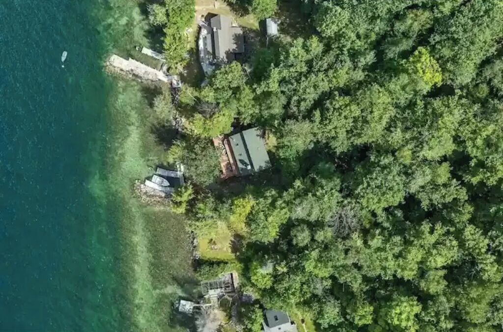 An aerial view of a coastal property with a house surrounded by dense greenery and a clear blue sea.