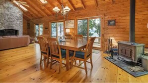 A wooden cabin interior with a dining area, stone fireplace, and a wood stove. - Waterfront at Winnipesaukee with incredible views!! Boat Required (Alton)