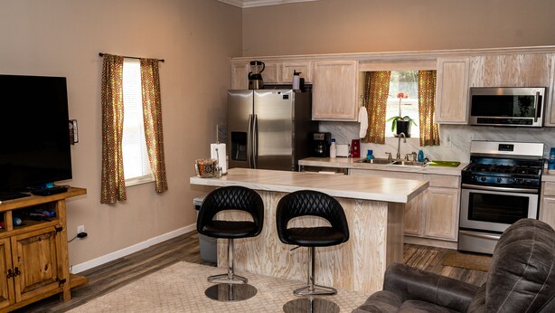 A modern kitchen with a refrigerator, microwave, stove, and bar stools. - Peaceful Paradise 3BR Cottage Getaway (Homer)