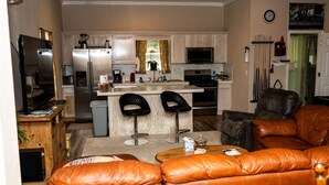 A compact living space with a kitchenette, two bar stools, a leather sofa, and a television. - Peaceful Paradise 3BR Cottage Getaway (Homer)