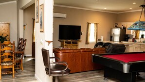 A living room with a pool table, a television, and a kitchen area. - Peaceful Paradise 3BR Cottage Getaway (Homer)