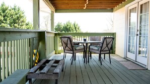 A covered outdoor patio with a wooden table and four chairs, a wooden bench, and a sliding glass door. - Peaceful Paradise 3BR Cottage Getaway (Homer)