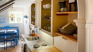 A kitchen with a wooden table and chairs, a sink, and shelves with dishes and glassware.