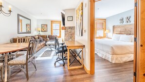 A room with a wooden dining table, chairs, a sofa, a bed, and a stone wall. - 1BD IN THE HEART OF RIVER RUN VILLAGE - 2 MIN. WALK TO GONDOLA (Keystone)