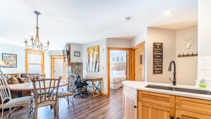 A spacious living area with a wooden dining table, chairs, and a chandelier. There is a kitchen with wooden cabinets and a sink. - 1BD IN THE HEART OF RIVER RUN VILLAGE - 2 MIN. WALK TO GONDOLA (Keystone)