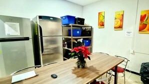 A kitchen with a refrigerator, a wooden table with a vase, and a shelf with blue bins. - HoM Balderas - Hostel (Mexico City)