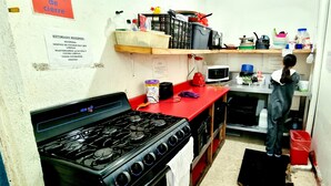 A compact kitchen with a gas stove, microwave, and various kitchen utensils on shelves. - HoM Balderas - Hostel (Mexico City)