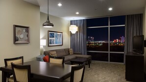 A hotel room with a dining table, chairs, a sofa, a TV, and a large window with a city view. - 1 Bedroom | Modern, Sophisticated Suite + Shuttles (Las Vegas)