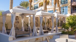 A rooftop lounge area with outdoor seating and umbrellas, surrounded by palm trees and a stone wall. - 1 Bedroom | Modern, Sophisticated Suite + Shuttles (Las Vegas)