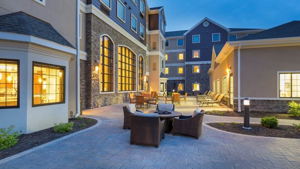 A courtyard with outdoor seating, stone walls, and multiple buildings with large windows. - 1 Bedroom | Breakfast Buffet. Pool & Hot Tub (Canton)