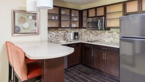A modern kitchen with dark wooden cabinets, a stainless steel refrigerator, a microwave, and a tiled backsplash. - 1 Bedroom | Breakfast Buffet. Pool & Hot Tub (Canton)
