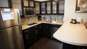 A modern kitchen with stainless steel appliances, dark cabinetry, and a tiled backsplash.