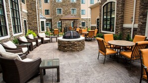 An outdoor patio area with wicker furniture, a stone fire pit, and a view of a multi-story building with large windows.