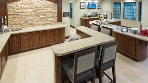 A bar area with granite countertops, wooden cabinets, and a stone accent wall. There are bar stools and a buffet setup with food and drinks.