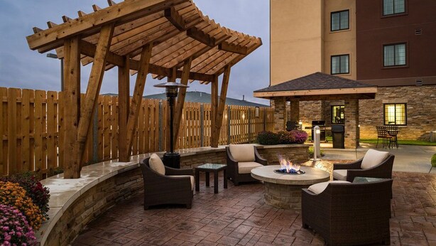 An outdoor patio with wicker furniture, a stone fire pit, and a wooden pergola.