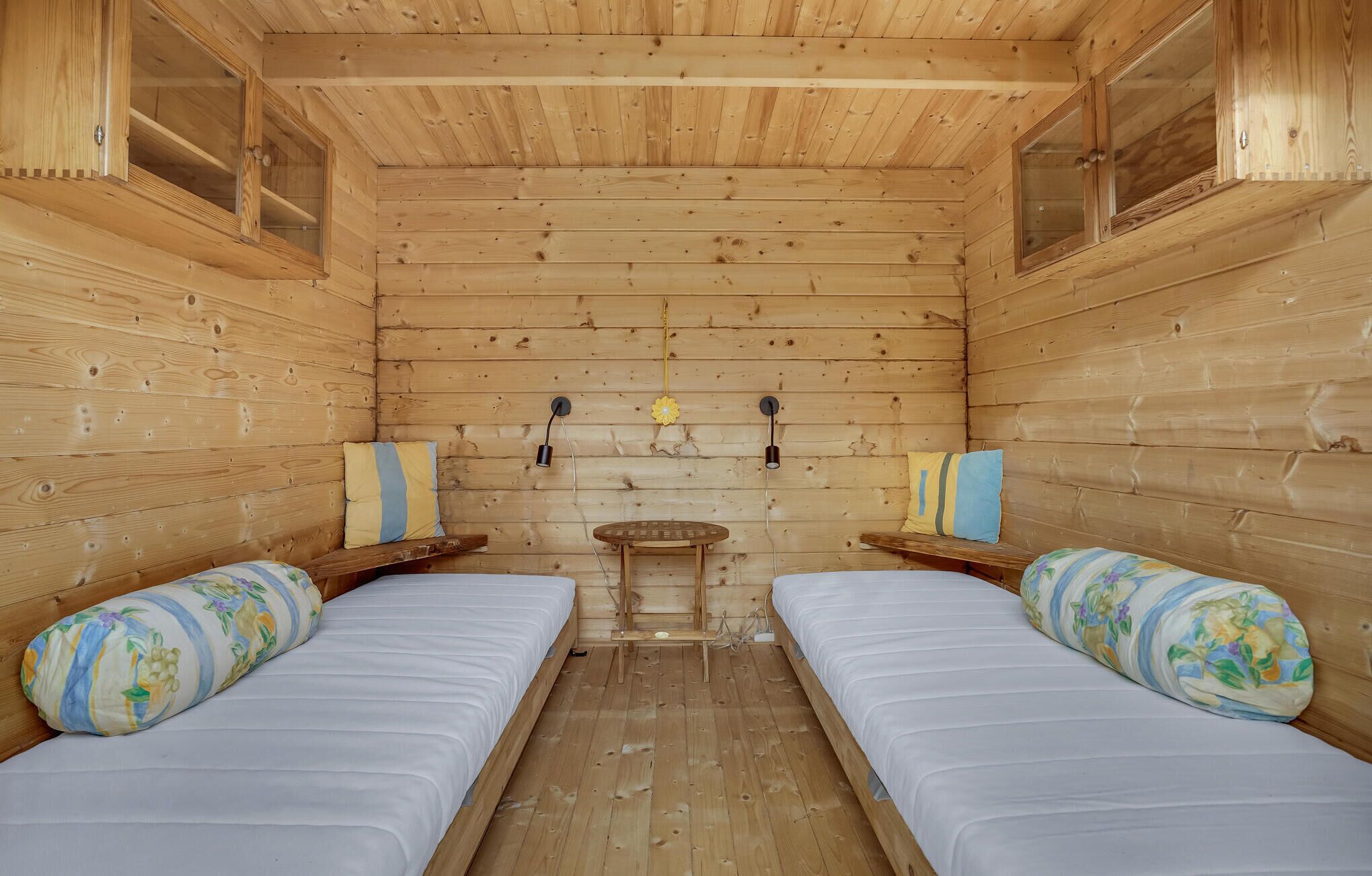Une cabine avec deux lits, des murs en bois, une petite table et deux lampes fixées au mur.