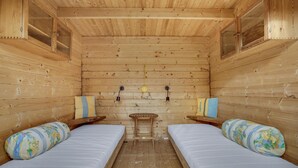 Uma cabana com duas camas, paredes de madeira, uma mesa pequena e duas luminárias fixadas na parede.